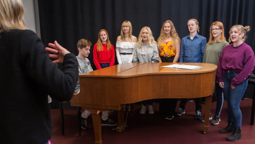 Elever står runt ett piano och en elev spelar på det