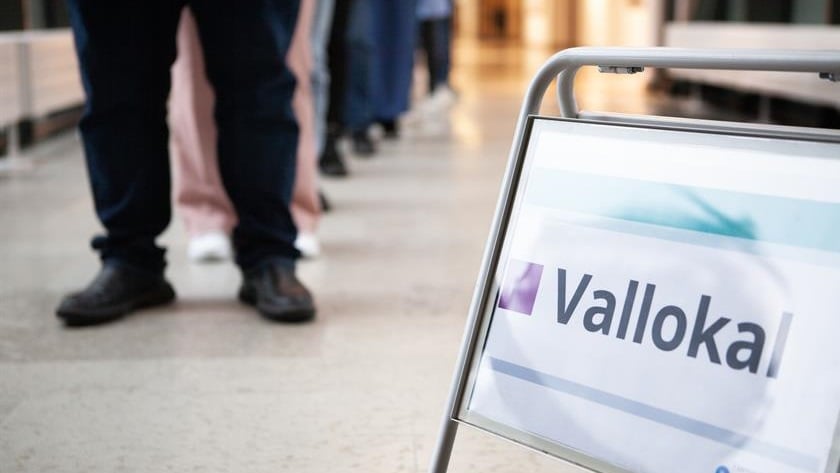 Skylt där det står vallokal och människor som står i kö bakom skylten