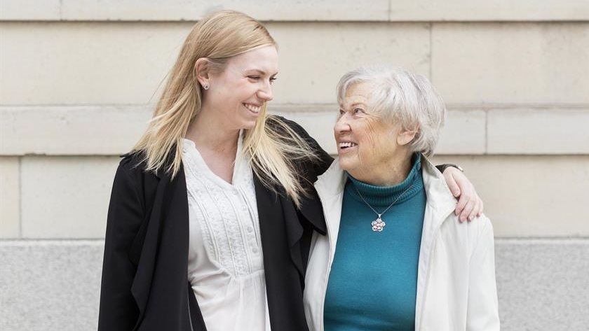En yngre person och en äldre person står bredvid varandra, tittar på varandra och är glada