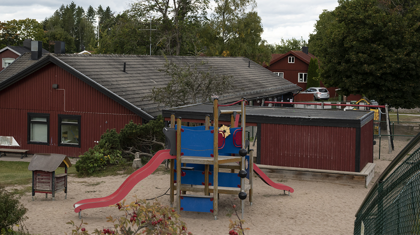 Bild på den röda förskolebyggnaden och lekställning