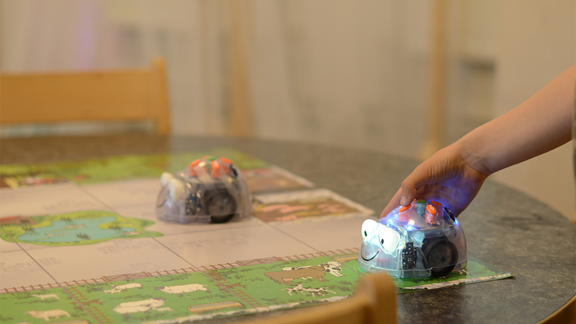 Bild på en liten körande robot med hjul och en barnhand som trycker på den
