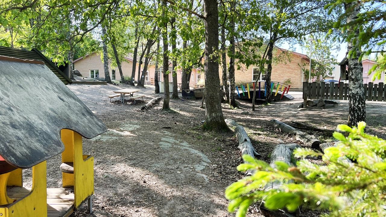 Gården på förskolan, från skogen med små hus och den röda tegelbyggnaden för förskolan i bakgrunden