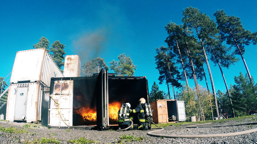 En brinnande övningscontainer och två brandmän utanför