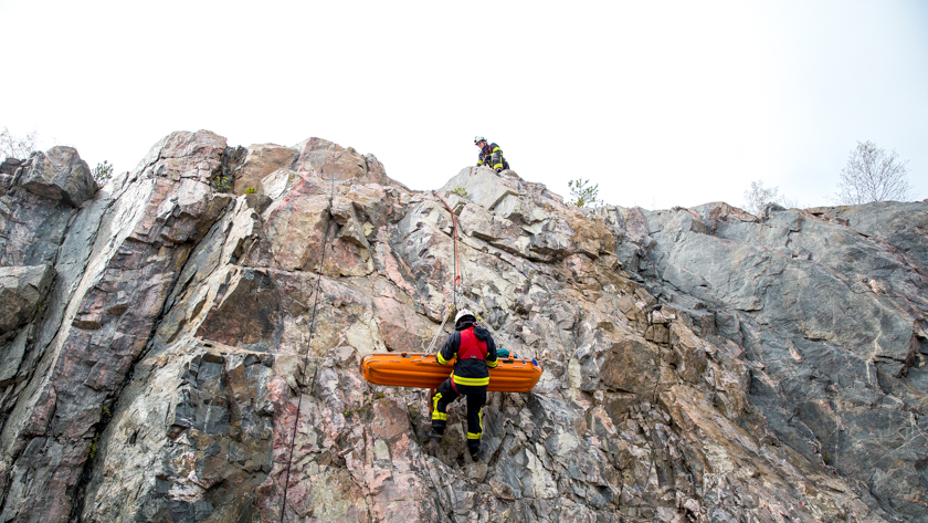 En brandman med en bår längs en bergvägg